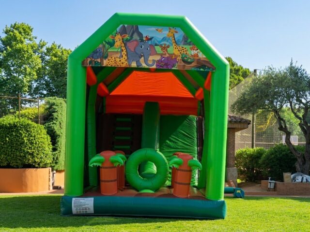 Combo hinchable Jungla con dibujos de jirafas y elefante, palmeras, obstáculos y tobogán en un jardín – Castillos Hinchables Madrid